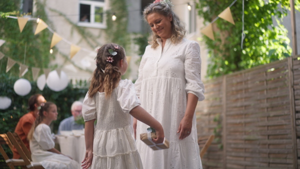 Rear view of little child giving wedding gift to mature bride at a wedding backyard party.