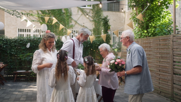 A mature bride and groom receiving congratulations at wedding reception outside in the backyard.