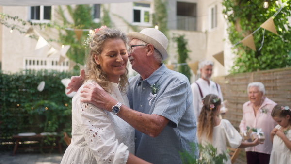 A mature bride receiving congratulations from her father at wedding reception outside in the backyard.