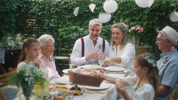 A mature bride and groom with guests at wedding reception outside in the backyard.