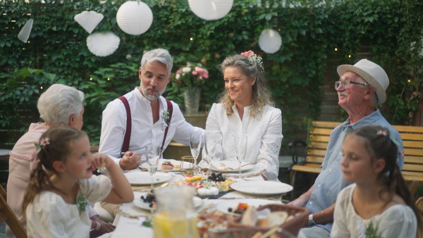 A mature bride and groom with guests at wedding reception outside in the backyard.