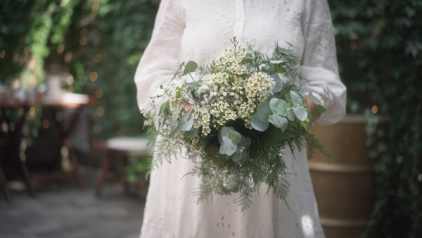 A close-up ofwedding bouquet in bride's hands at reception outside in backyard