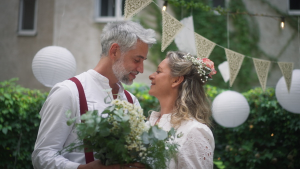 A mature bride and groom having a romantic moment at wedding reception outside in the backyard.