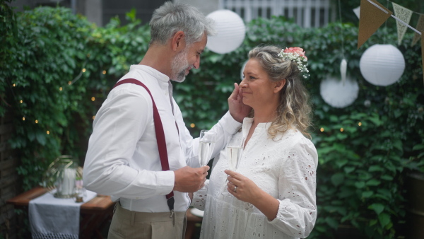 A mature bride and groom toasting at wedding reception outside in the backyard.