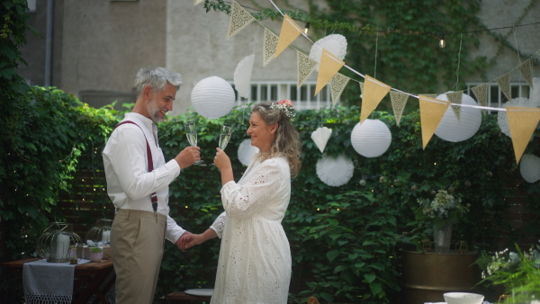 A mature bride and groom toasting at wedding reception outside in the backyard.