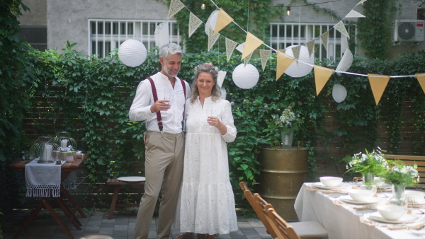 Mature bride and groom toasting with their daughters at wedding reception outside in backyard.