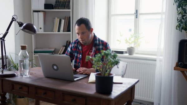 A young man with Down syndrome sitting at desk at home and using laptop.