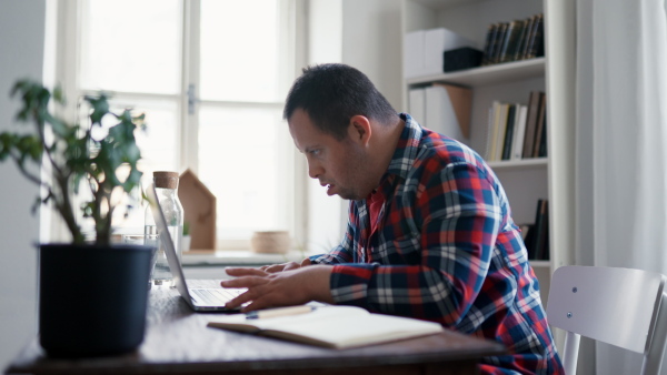 A young man with Down syndrome sitting at desk at home and using laptop.