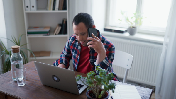 A young man with Down syndrome sitting at desk at home using laptop and smartphone,homeoffice concept.