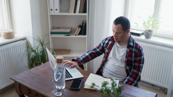 A young man with Down syndrome sitting at desk at home and using laptop.