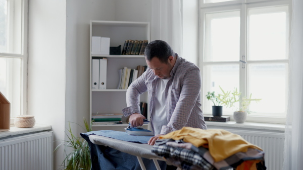 An independent young man with Down syndrome and ironing clothes at home.