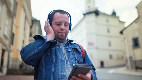 A happy young man with Down sydrome listening to music when walking in street.