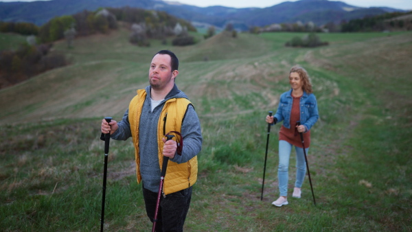 Happy young man with Down syndrome and his mother hiking together in a nature.