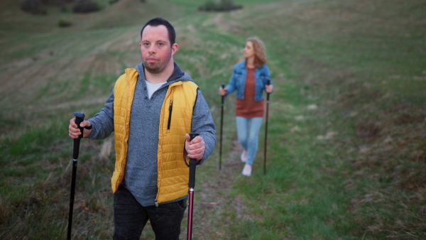 Happy young man with Down syndrome and his mother hiking together in a nature.