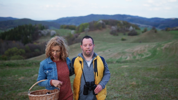 A happy young man with Down syndrome with his mother resting in nature, walking and looking at view trough binoculars.