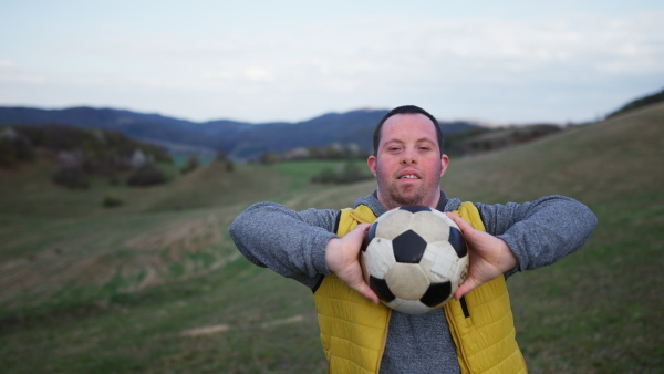 Happy young man with Down syndrome playing with a soccer ball in nature, showing his skills.