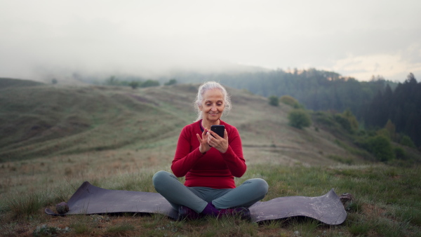 A senior woman taking selfie in nature on early morning with fog and mountains in background.