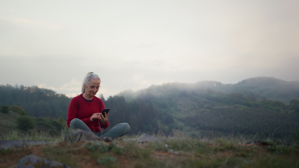 A senior woman taking selfie in nature on early morning with fog and mountains in background.