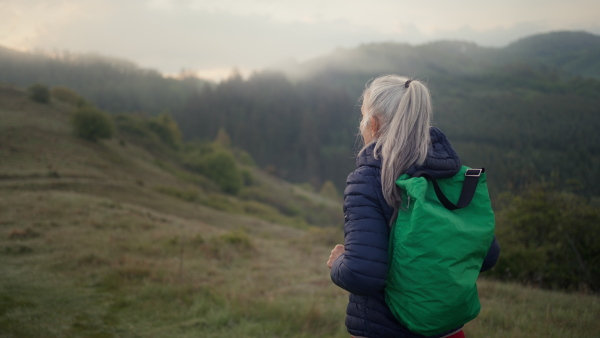 A senior woman hiking in nature on early morning with fog and mountains in background.