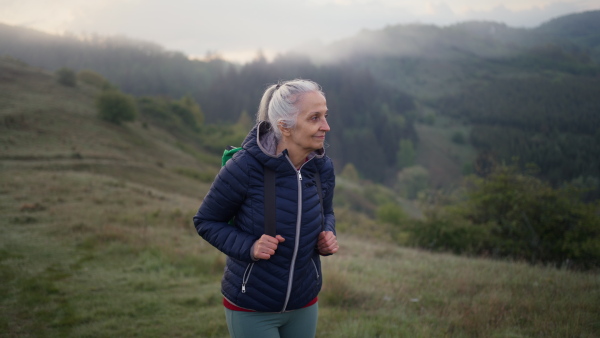 A senior woman hiking in nature on early morning with fog and mountains in background.