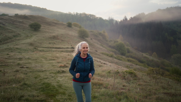 A senior woman jogging in nature on early morning with fog and mountains in background.