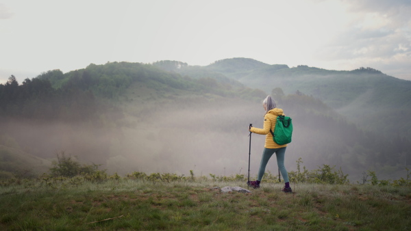 A senior woman hiking in nature on early morning with fog and mountains in background.