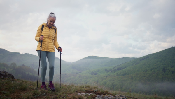 A senior woman hiking in nature on early morning with fog and mountains in background.