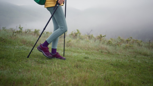 A senior woman hiking in nature on early morning with fog and mountains in background, legs close-up.