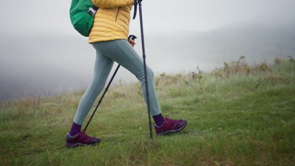 A senior woman hiking in nature on early morning with fog and mountains in background, legs close-up.