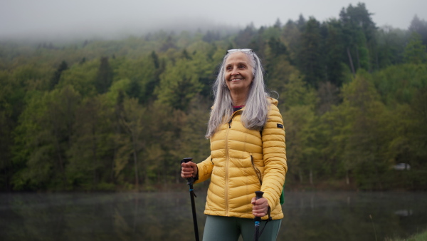 A senior woman hiking in nature on early morning with fog and mountains in background.