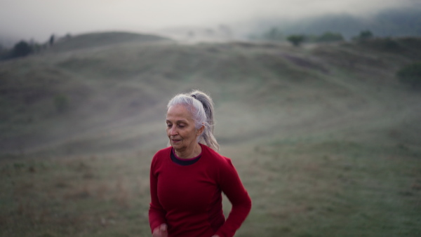 A senior woman jogging in nature on early morning with fog and mountains in background.