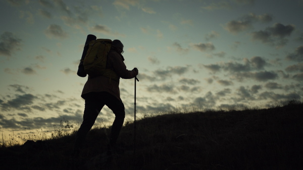 Male hiker walking up a hill at sunrise. Silhouette with clouds in background.