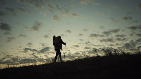 Male hiker walking up a hill at sunrise. Silhouette with clouds in background.