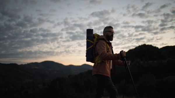 Mature man looking at view at top of a mountain at dusk.