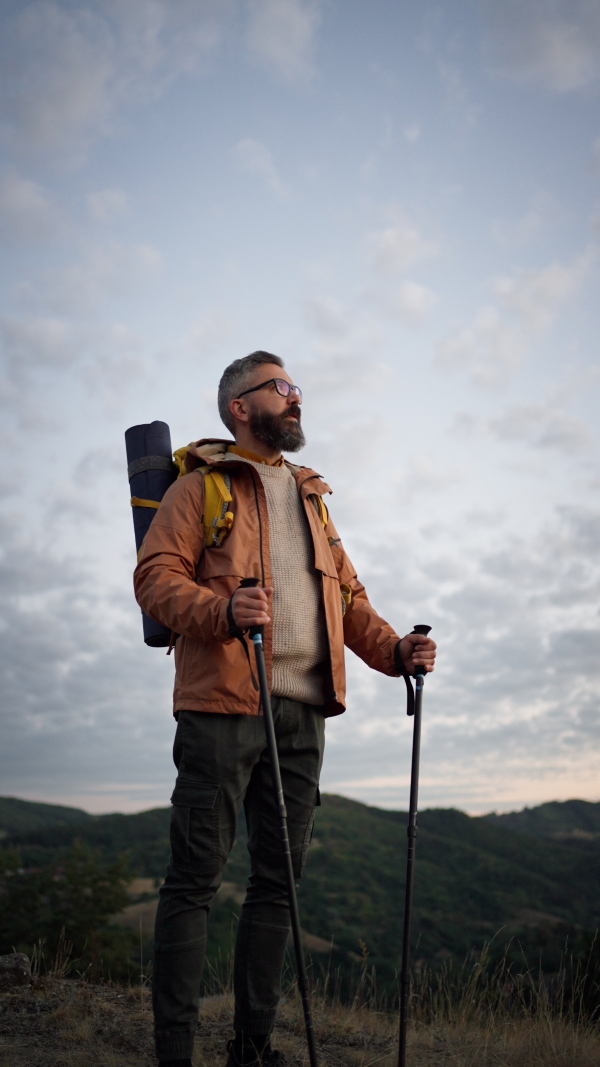 Mature man looking at view at top of a mountain at dusk. Vertical shot.