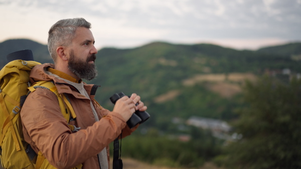 Mature male hiker looking through binoculars in natural environment.