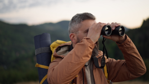 Mature male hiker looking through binoculars in natural environment.