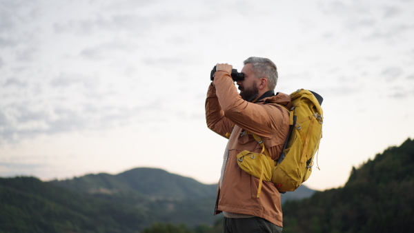 Mature male hiker looking through binoculars in natural environment.