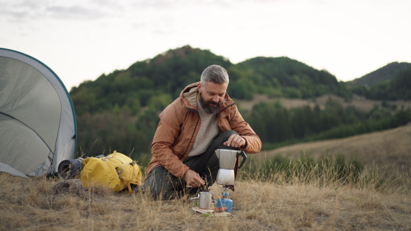 Hipster man at hike, smelling fresh made coffee from kettle.