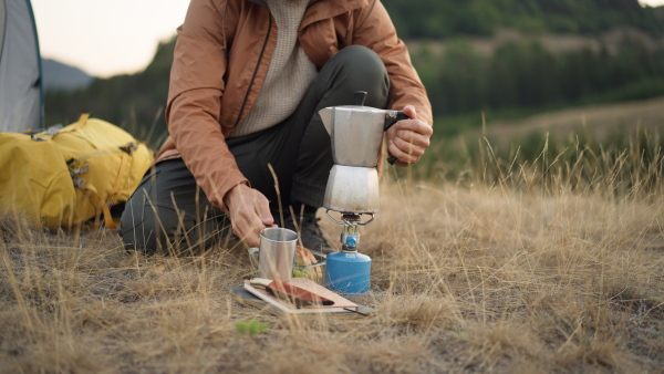 Unrecognizable man at hike, pouring coffee into cup while having a pause in nature.