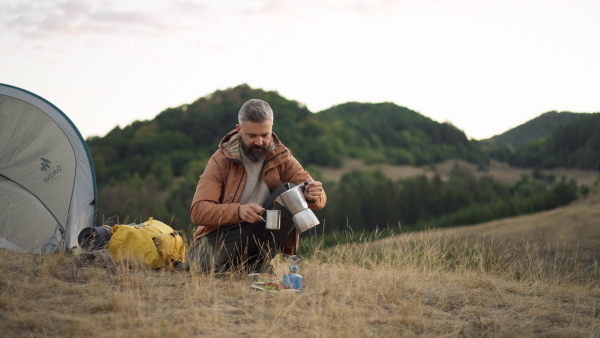 Male hiker pouring fresh made coffee from percolator into cup in nature.