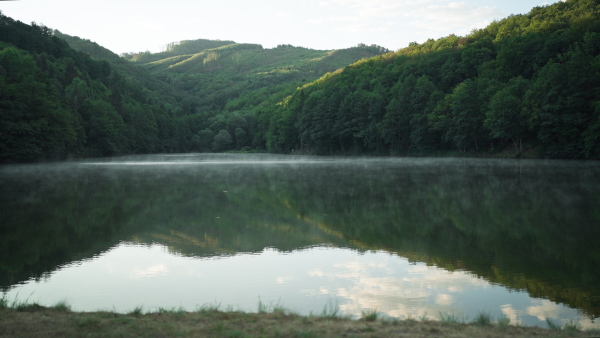 Water surface of natural lake at morning with misty haze and reflection of mountains.