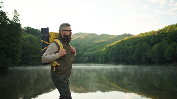 Male hiker wearing backpack walking at a lake looking at the beautiful surroundings.