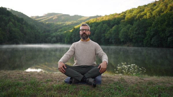 Mature man meditating at lake in peceful natural surrounding.