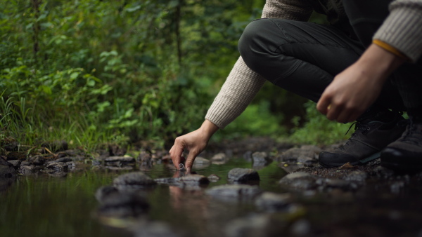 Close up of unrecognizable man taking water samples from river in forest.