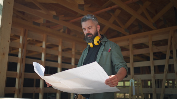 Man looking at construction plans on building site of wooden sustainable house.