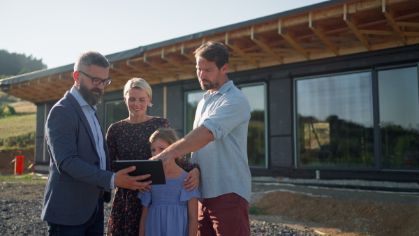 Family consulting new home with architect on building site in front of of sustainable house.