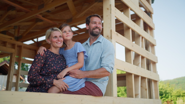 Joyful family enjoying the view from their new future home on construction site of sustainable house. Natural environment.