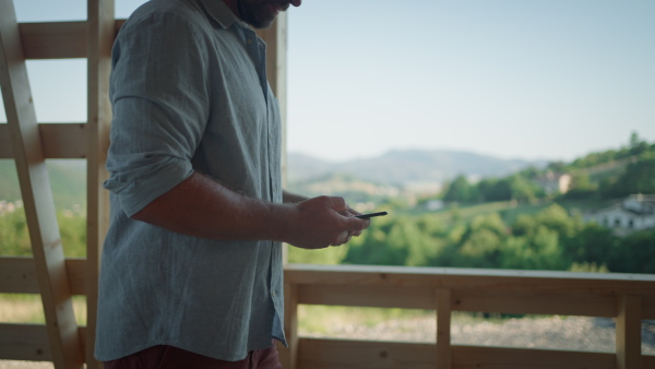 Man making phonecall on construction site of new sustainable home looking at natural view.