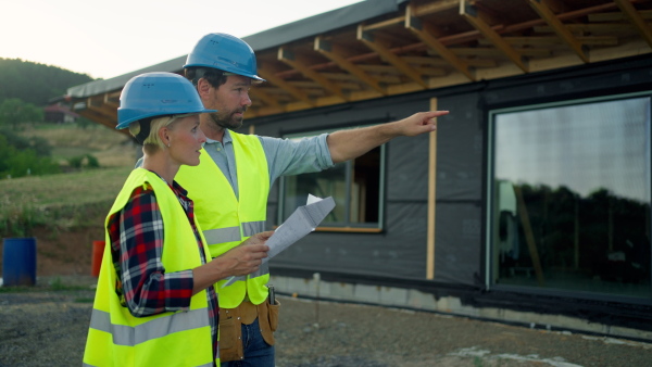 Female architect and male worker consulting plans on construction site of sustainable home.